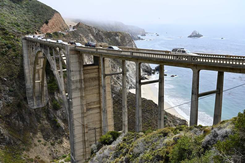 a narrow bridge crosses a canyon above a rocky beach