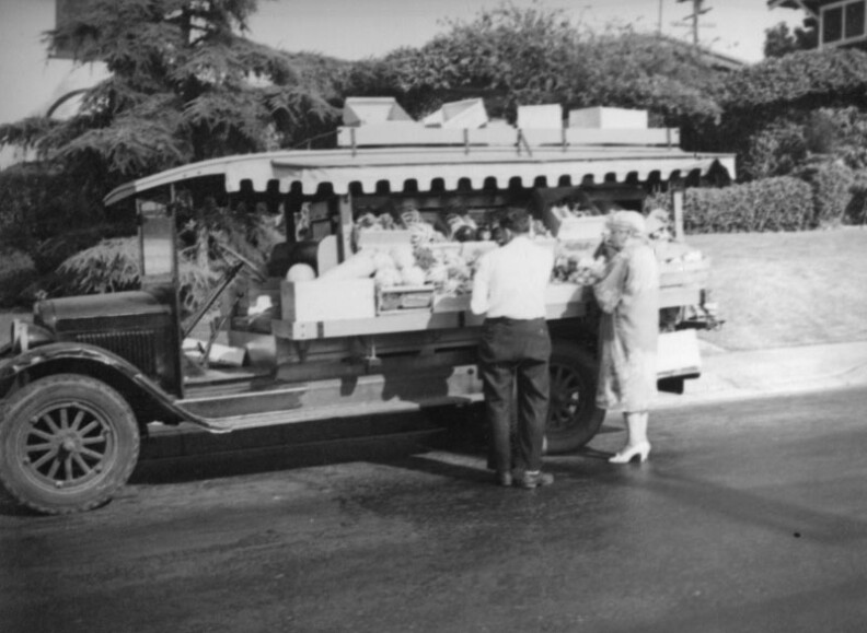 A man, probably the vendor, assists a woman standing in front of a truck parked in a residential neighborhood of Los Angeles, circa 1937. 