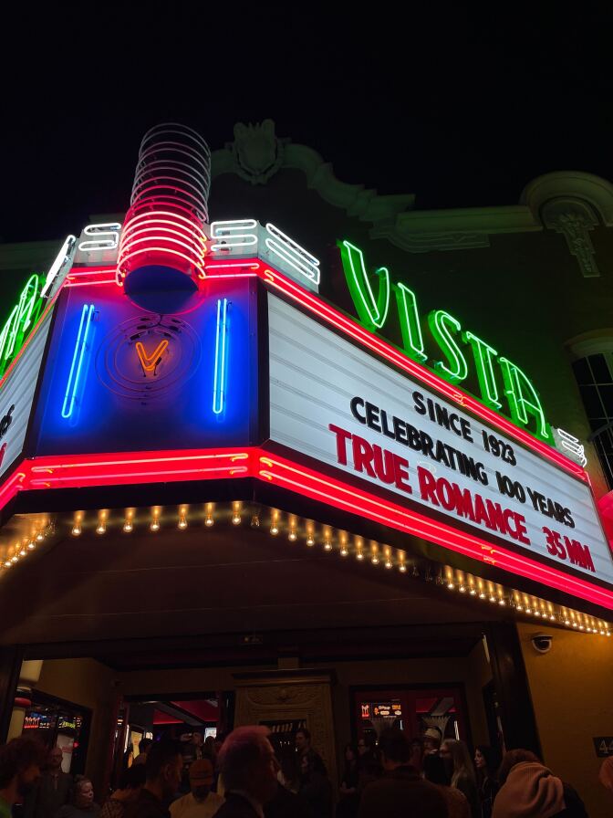 Looking up at the marquee of the Historic Vista Theater in Los Feliz. It's lit up in neon green and red with signage that reads:  

Since 1923 
Celebrating 100 Years 
True Romance 35MM"