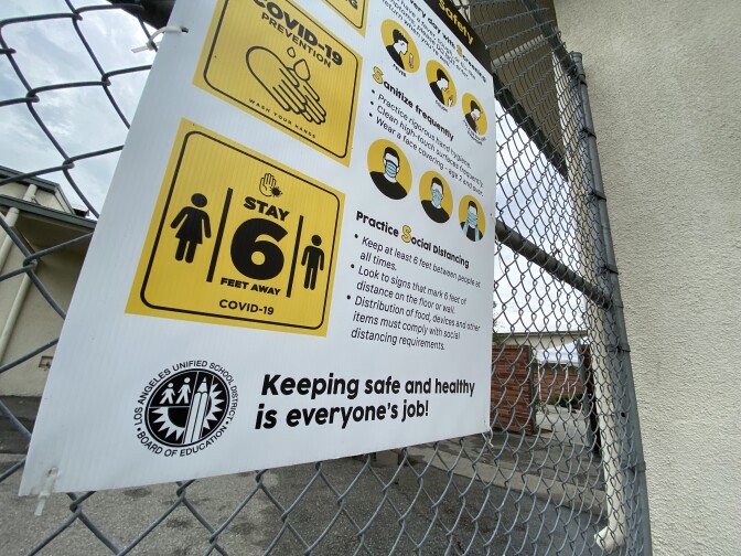 A sign posted on a chain-link fence reads: "Keeping safe and healthy is everyone's job!"
