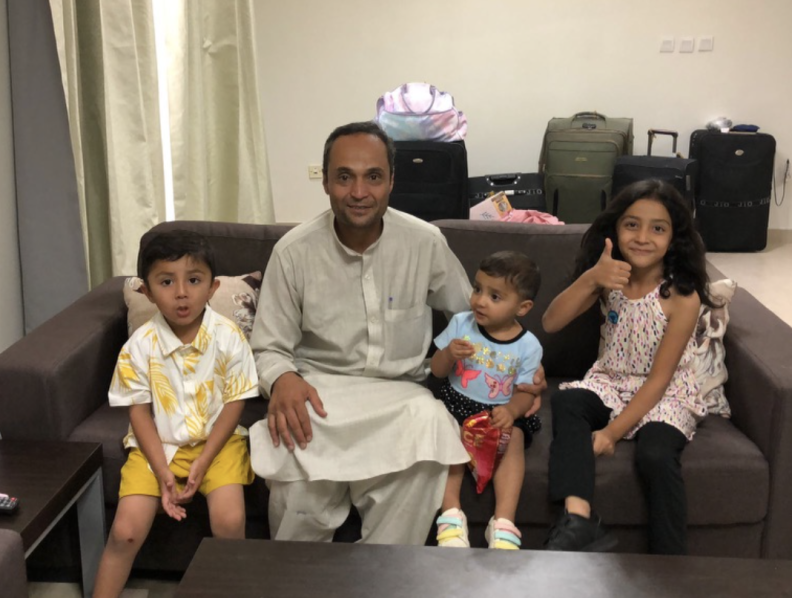 A man and three young children sit on a brown sofa.