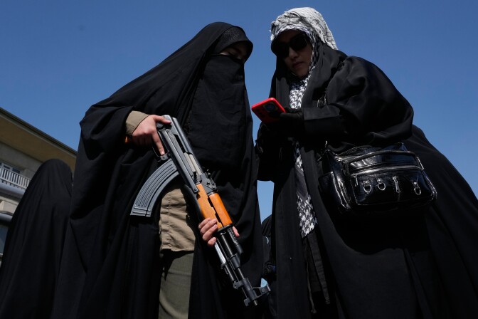 Two women dressed in all black, with one woman holding a machine gun.