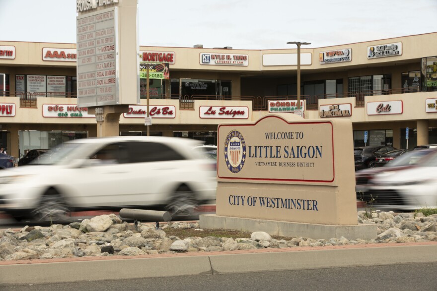 A white vehicles zooms past a street sign that reads Welcome to Little Saigon, City of Westminster.