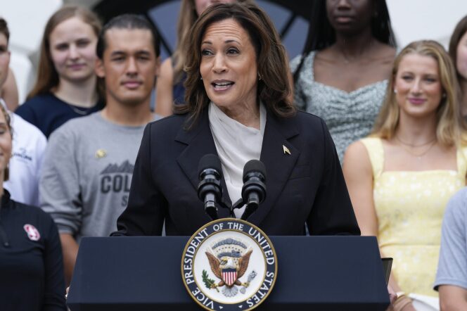 A female-presenting person with brown hair and medium-dark skin tone wearing a navy blazer and white blouse speaking into a microphone at a podium which bears the presidential seal. 