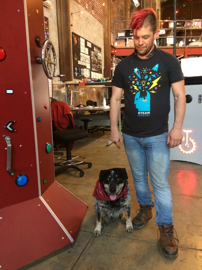 Eric Gradman stands next to the Gadgettron (red obelisk with buttons) with his trusty Chief of Security, Bronco at his side. 