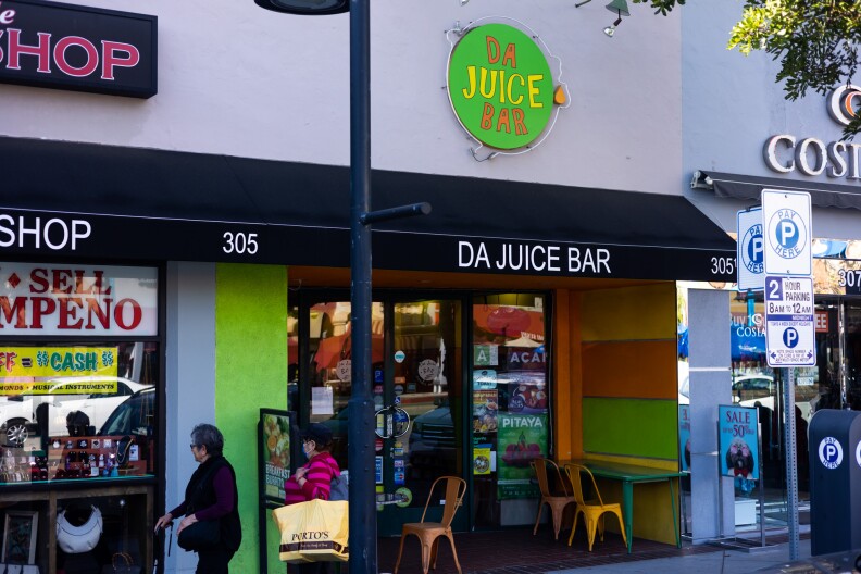 An entryway of a small juice bar. It's painted yellow, orange, and green on the inside, with a few tables and chairs that are painted yellow on the outside.