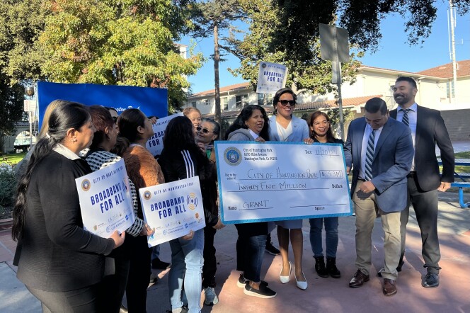 A group of people are  smiling and celebrating as they hold up a large check addressed to the city of Huntington Park.