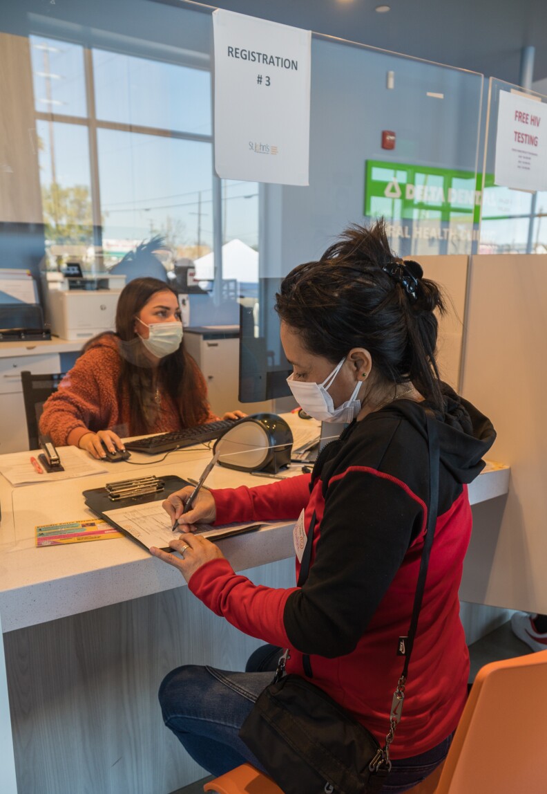 LA Community Clinics Vaccinate The Most Vulnerable. A Year Later, They Still Haven't Been Paid. - LAist 3 A masked woman fills out a form at the check in counter of the St. John's Avalon clinic in South L.A. A masked employee sits behind the counter, using a computer.