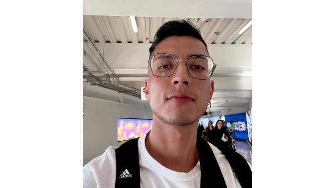 A selfie of a brown-skinned Latino man wearing glasses in an airport. 