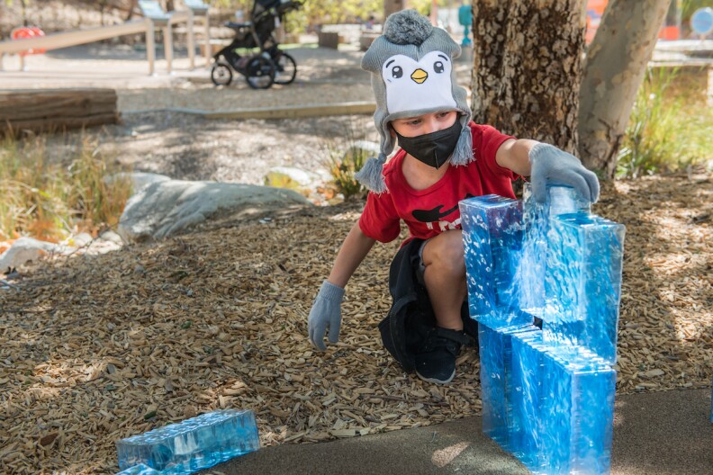 a child in a penguin hat builds a sculpture with blocks of ice