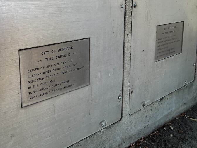 A close up of a metal door with a metal placard that reads "City of Burbank Time Capsule. Sealed on July 4, 1977, by the Burbank Bicentennial Committee. Dedicated to the citizens of Burbank in the year 2026. To be opened during their Independence Day celebration."