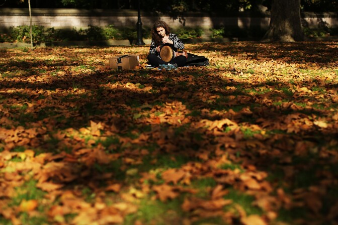 A woman plays a drum surrounded by fallen leaves as autumn foliage fills the trees of Prospect Park on October 30, 2015 in the Brooklyn borough of New York City.