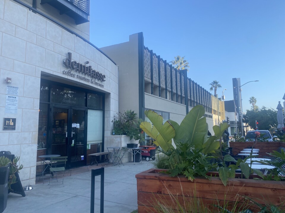 The exterior of Demitasse on 3rd Street in Santa Monica: The exterior is accented with beige, stone tiles and the overall vibe is modern. There is patio seating outside. 