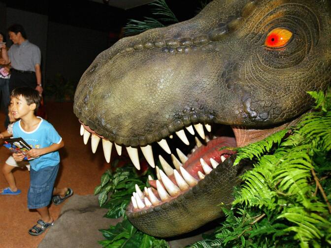 Children run away from a dinosaur at a "Jurassic Park: The Ride" display set up in a Tokyo department store on August 11, 2004 to promote Universal Studios Japan.