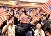 A crowd of mostly Asian Americans at a concert hall wave American flags.