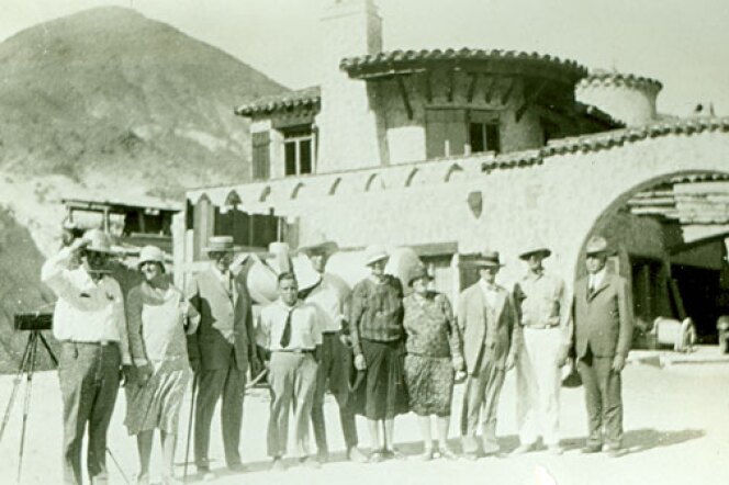 A group of people standing in front of a mansion in the desert.