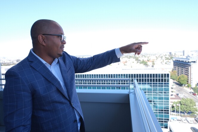 Long Beach Mayor Rex Richardson, the board chair of LACAHSA, stands on a city hall balcony and points to a housing project under construction.