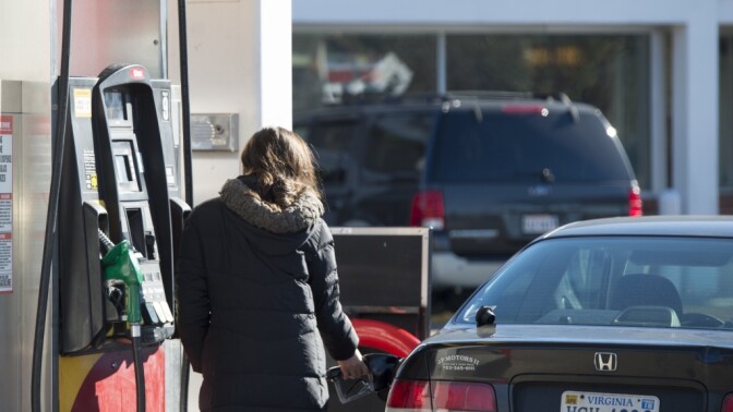 A woman fills her car with gas in Woodbridge, Va., on Tuesday. Supplies of crude oil and refined gasoline have driven prices at the pump down, and they're  expected to go even lower.