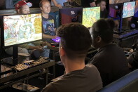 A group of people sitting in front of monitors and playing Street Fighter 6.