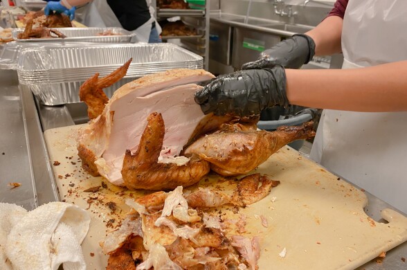 A close up of hands with black gloves carving a large cooked turkey on a chopping board.