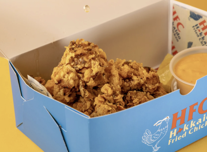 A close up of a blue box which says HFC Hokkaido fried chicken. Inside is a piece of fried chicken that is brown and craggy looking