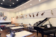 The dining room at Chopin Noodle House in Monterey Park. White tables and wooden chairs fill the room, next to a black baby grand piano with its lid propped open. A wavy white wall above displays violins, a saxophone, a trumpet, a harp and a gramophone. Colorful cubist paintings of a cat and of Chopin at the piano hang on the back wall.