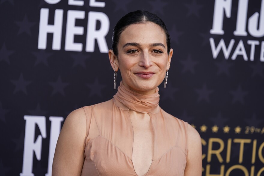 A woman is smiling, looking off to the distance. She's wearing a translucent dress and hooped earrings.