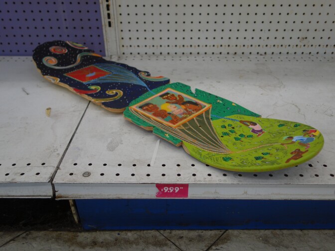 A skateboard with no wheels or axels on the bottom of store shelving.