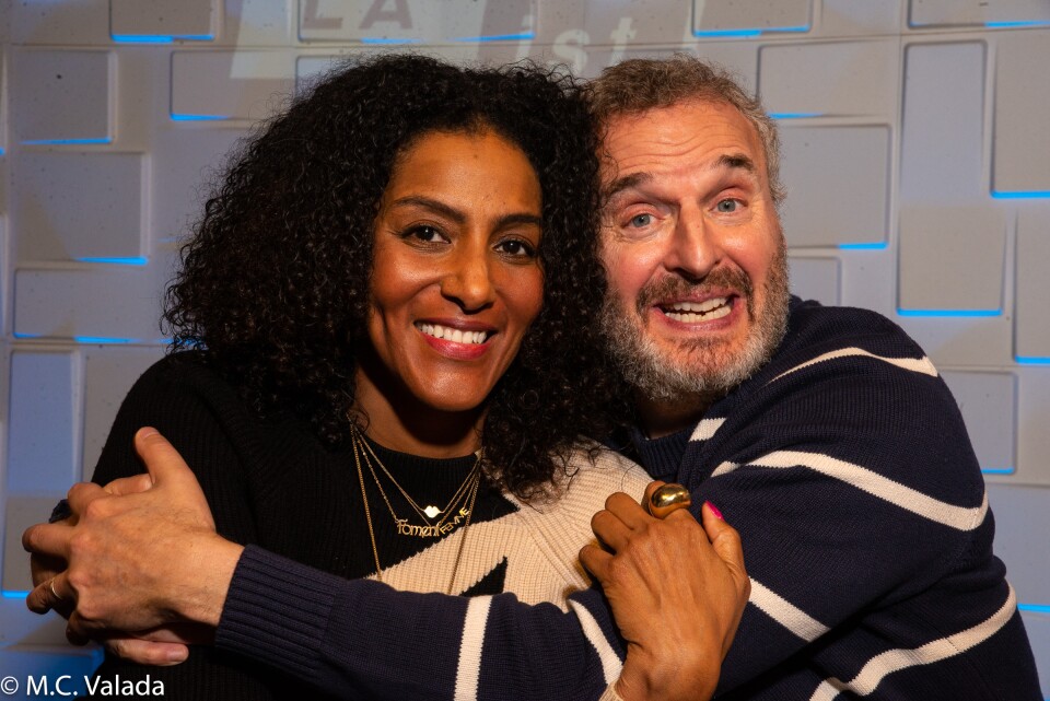 Sarah Jones, a dark-skinned woman, and Phil Rosenthal a light-skinned man with a beard hugging and smiling at the camera