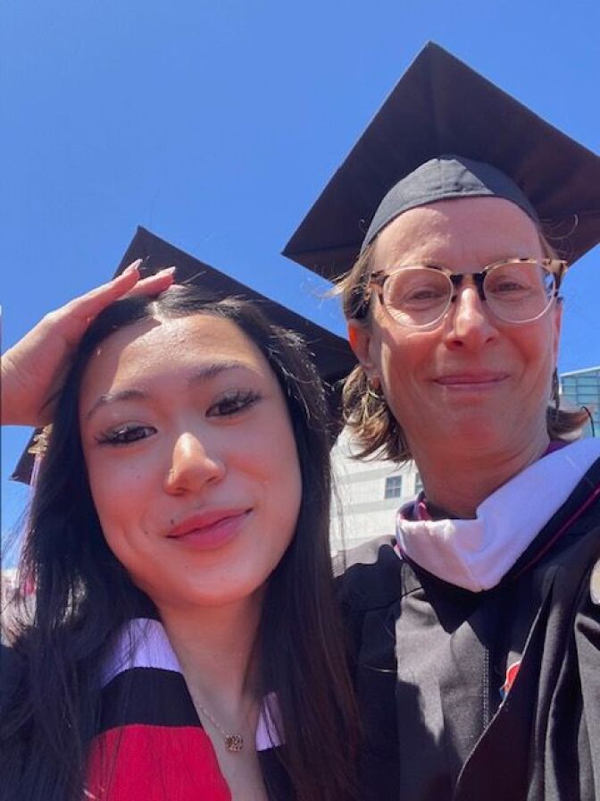 A graduate and a faculty member smile for a selfie in caps and gowns.