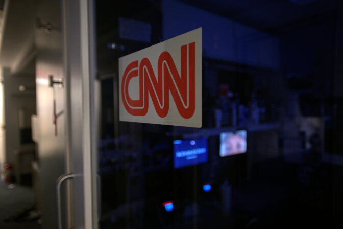 A logo for "CNN" in red and white, placed on a tinted glass door.