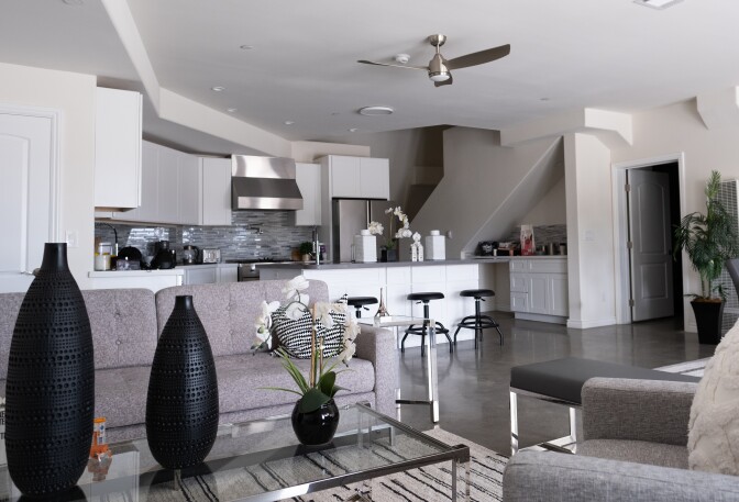 A grey and white living room and kitchen with black accented furniture and decorations.