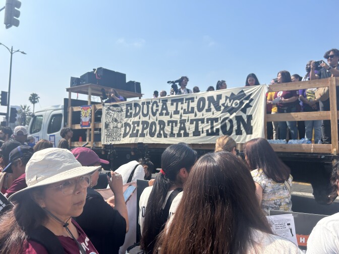 A banner hangs over the side of a truck and reads "Education Not Deportation". People are standing below the truck and on the truck. 