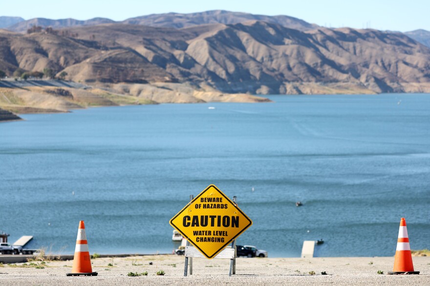 A yellow caution sign reads: Beware of hazards, water level changing. Next to it are two orange traffic cones.