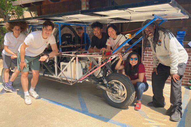 Seven people of various skin tones pose for a photo with their solar power buggy.