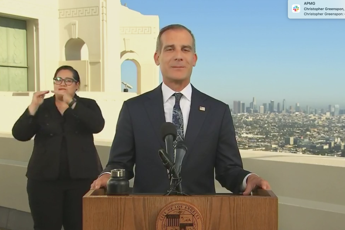 L.A. Mayor Eric Garcetti stands at a podium with the city's seal. He's speaking at the Griffith Observatory, and a view of Los Angeles stretches out behind him. Over his right shoulder, a sign language interpreter performs the speech for the hearing impaired.