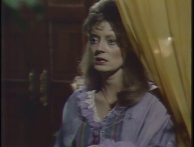 a woman in a frilly lavender nightgown stands next to a curtain. she looks worried and scared