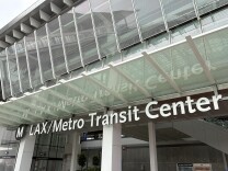 A black and white sign with an "M" representing L.A. Metro's logo followed by "LAX/Metro Transit Center" The sign reflects on the glass above it. 