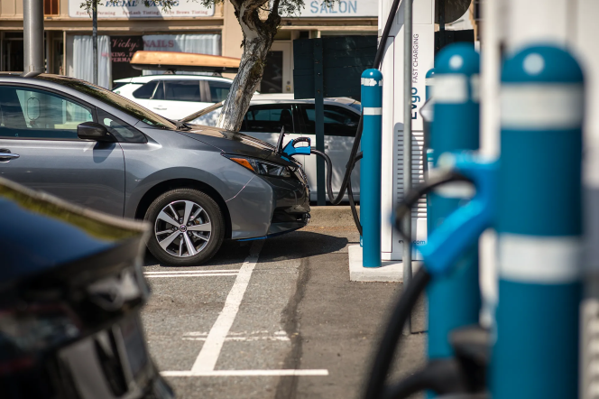 A gray sedan is connected to a charger at an electric vehicle charging station. 