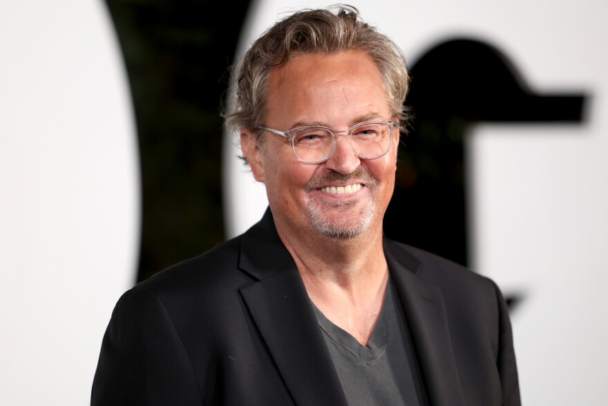 A man with light-tone skin has clear-framed glasses and a gray facial hair.