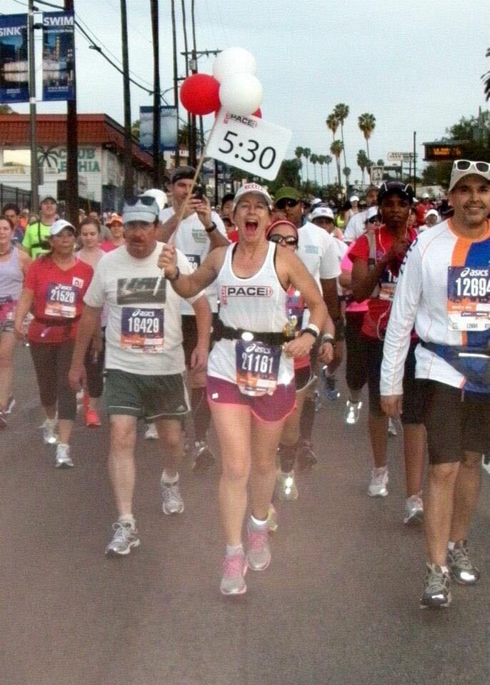 A woman in runner's tanktop and shorts holding a sign that says 5:30. She is leading a group of runners and walkers.