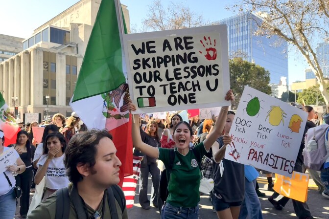 A teenage girl, surrounded by other teenagers, holds up a sign that says "We are skipping our lessons to teach u one."