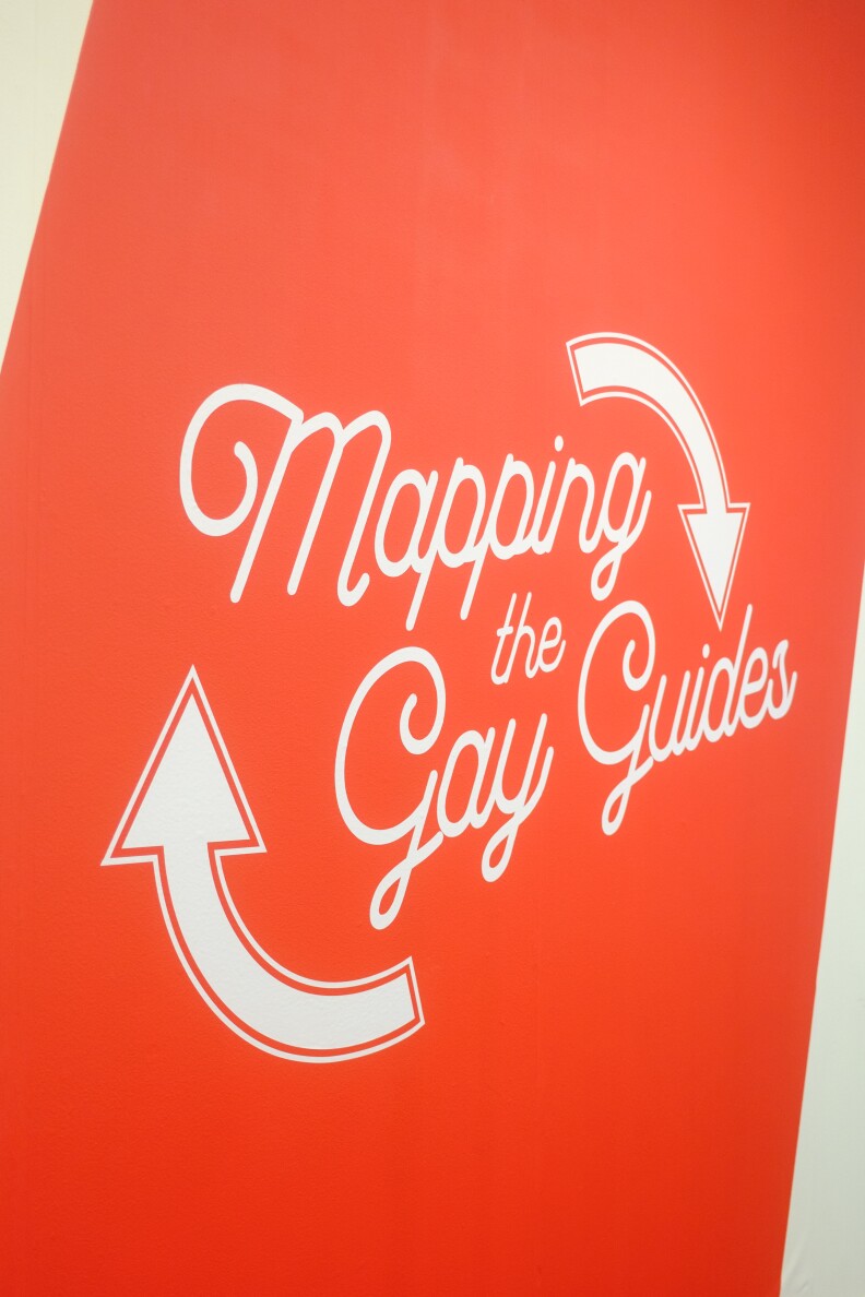 A red wall with white letters reading "mapping the gay guides"