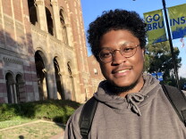UCLA student with glasses in front of red brick building. 