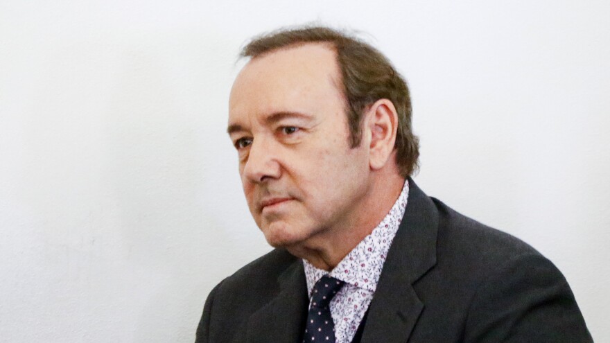 Kevin Spacey wears a floral patterned shirt and tie with a dark suit coat.