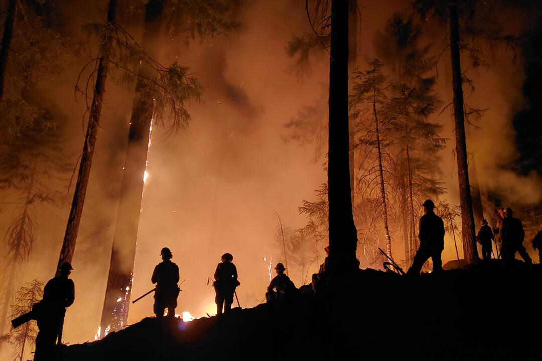 Firefighters are silhouetted on ridge with the sky full of red smoke