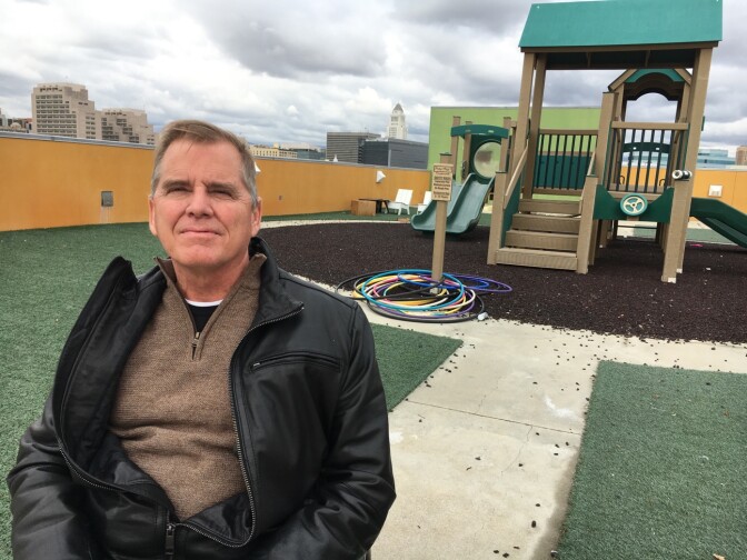 A white man in a dark jacket and pullover poses in front of a new children's playground