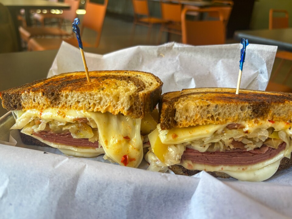 A close-up of a Reuben sandwich cut in half, with slices of corned beef, melted Swiss cheese, sauerkraut, and Russian dressing layered between toasted marble rye bread. Toothpicks hold each half together as melted cheese drips invitingly over the edge. 