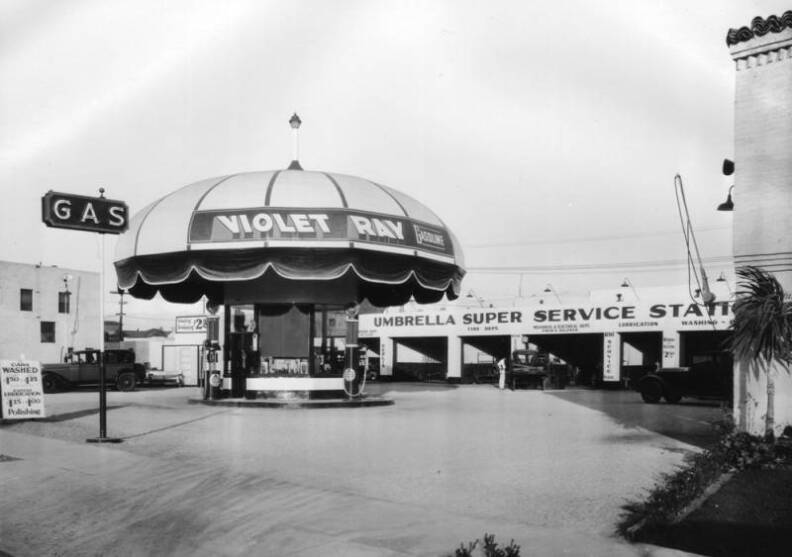 A black and white photo of a gas station shaped like a giant umbrella.