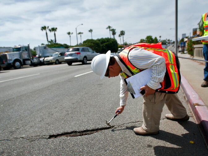 Senior Bridge Engineer Bing Wu uses a hammer to inspect a crack in the bridge's asphalt. Then he measures how long and deep the hole is.